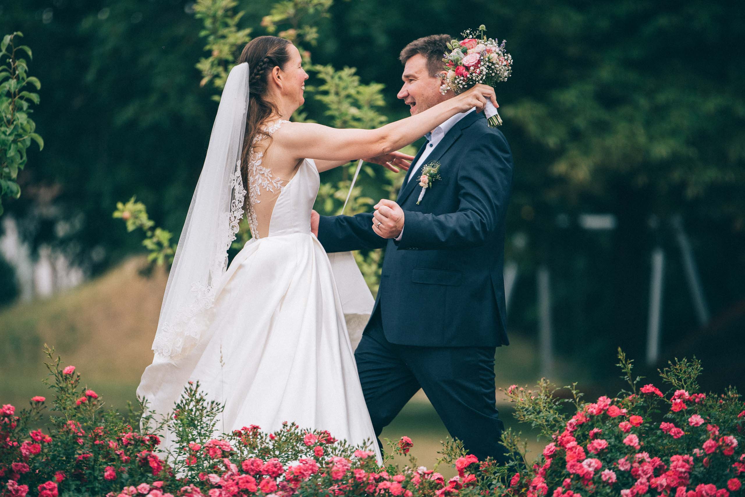Foto aus einer Hochzeitsreportage. Das Brautpaar steht in einem Rosengarten und fällt sich verliebt in die Arme.