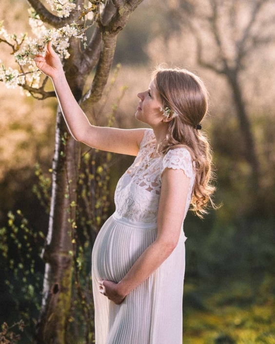 Eine schwangere Braut im Brautkleid greift während des Couple Shootings nach einer Kirschblüte