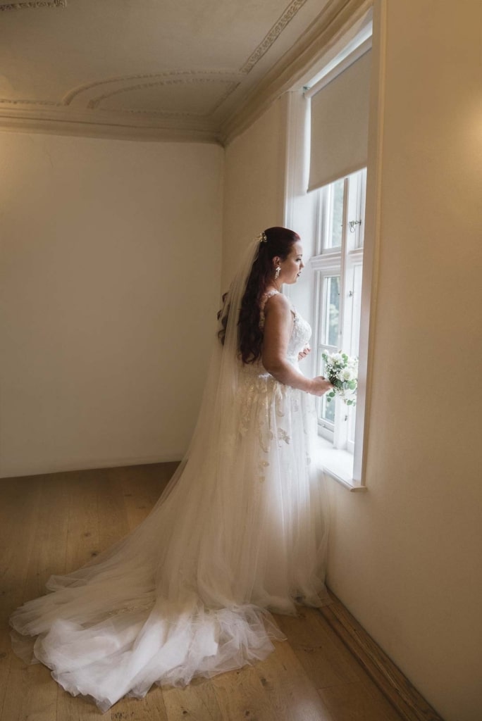 Braut schaut vor ihrer Hochzeit in Wolfsburg verträumt aus dem Fenster