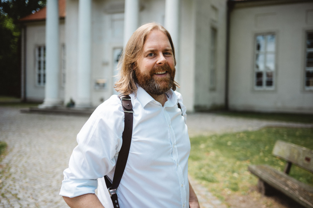 Hochzeitsfotograf Marc Beierstedt posiert lächelnd vor einer Kirche