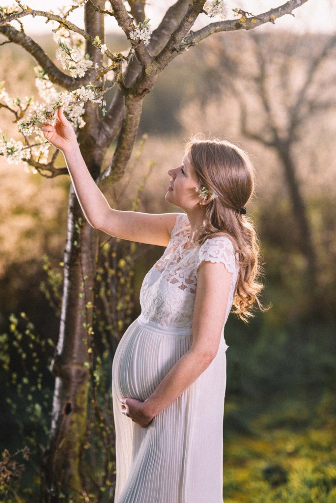 Braut mit Babybauch im Hochzeitskleid pflückt eine Kirschblüte