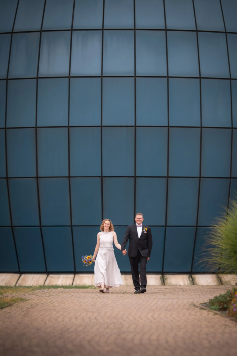 Brautpaar läuft Hand in Hand vor dem Planetarium Wolfsburg